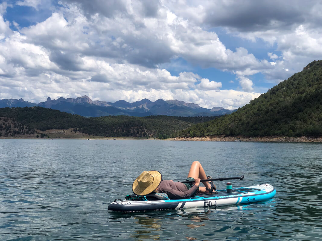 A paddle boarder soaking in the warm mid-summer sun while floating in the blue-green waters at Ridgeway Reservoir. 