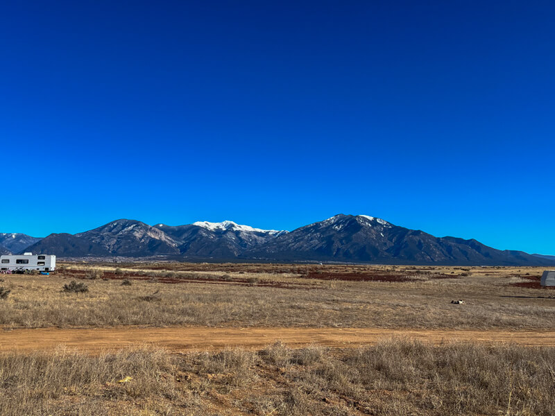 A large desert mesa on a cloudless day with snow-capped mountains in the background. 