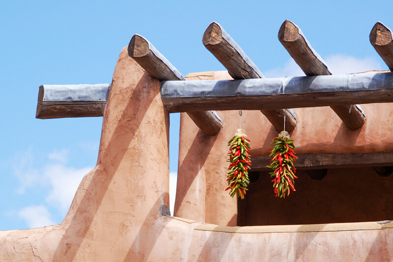 A traditional style adobe building with dried chile ristras hanging from the wooden vigas. 